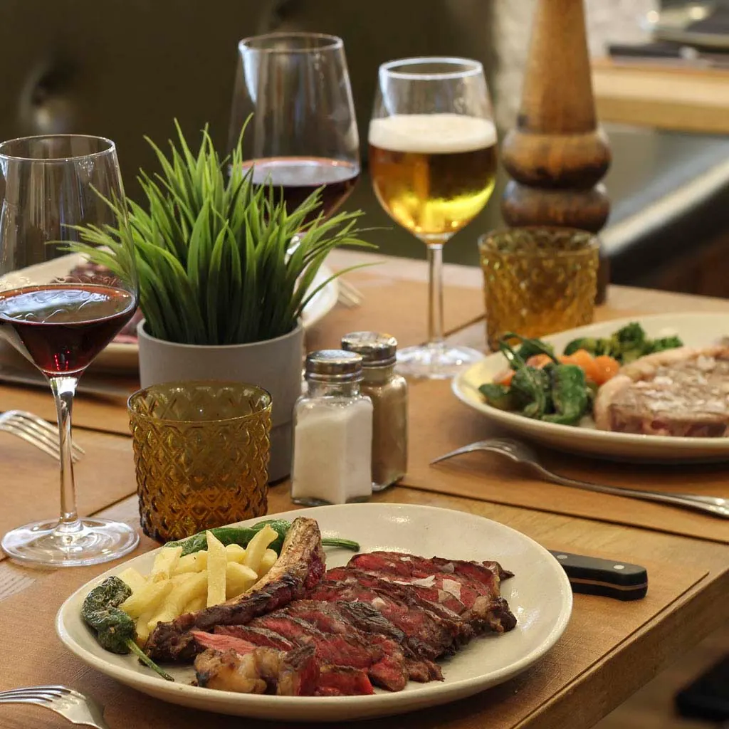 Mesa con carne de vaca vieja a la brasa, patatas fritas y copas de vino en The Beefeater